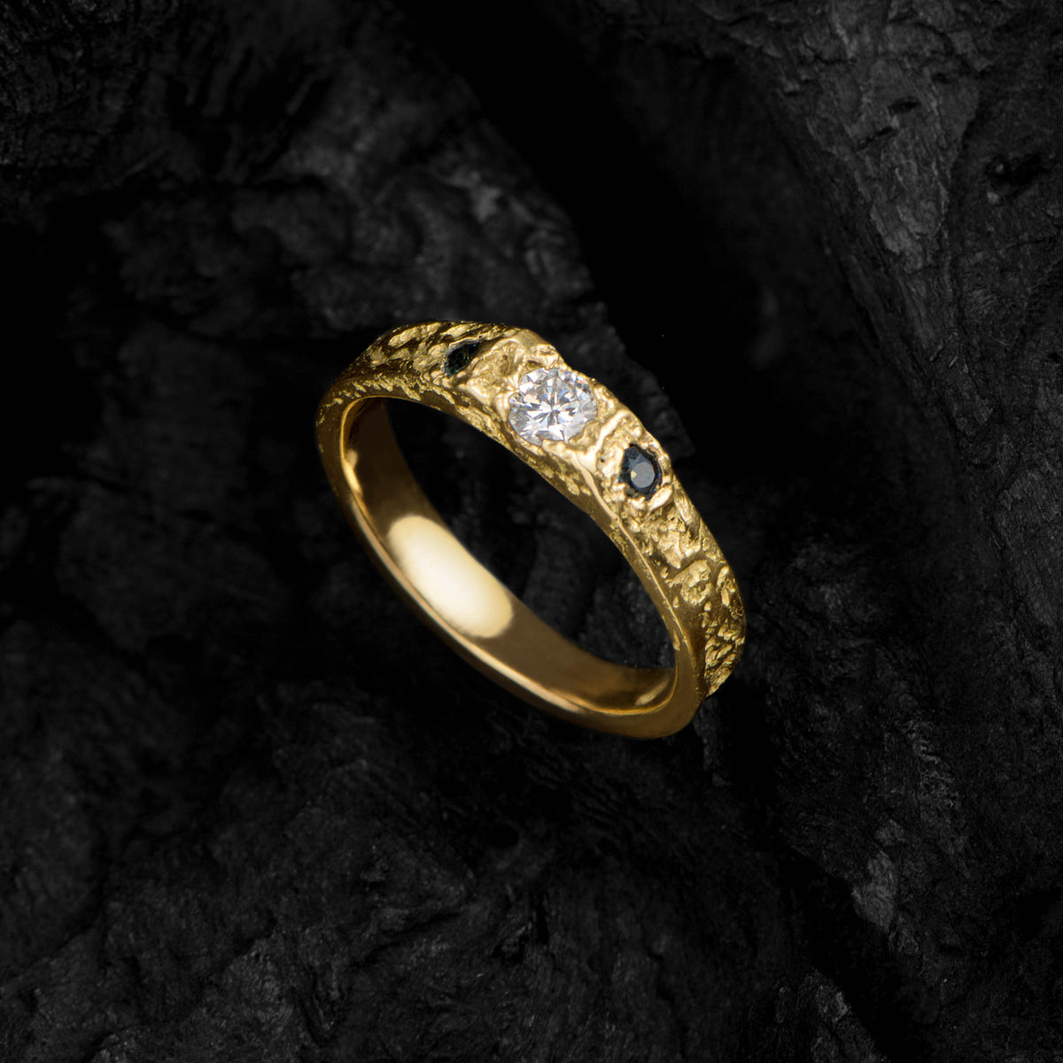 Gold ring with a diamond and black gemstone on a dark textured background