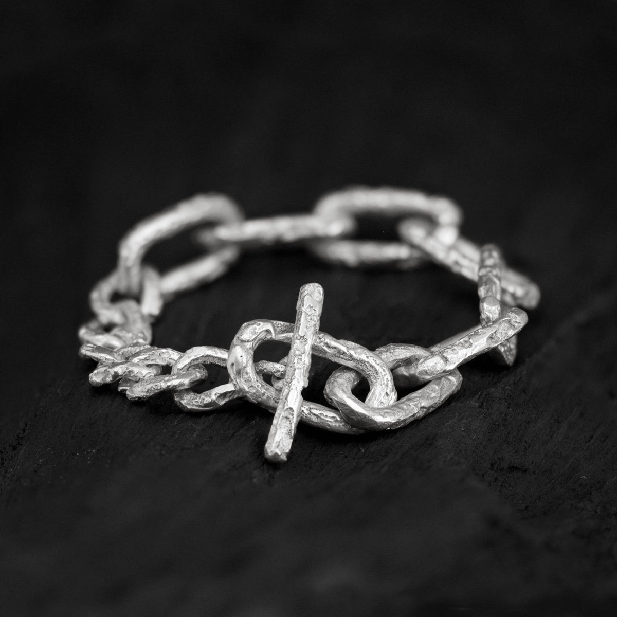 Sterling silver link chain bracelet with a big toggle clasp and lots of texture, handcrafted in Berlin on a dark background.