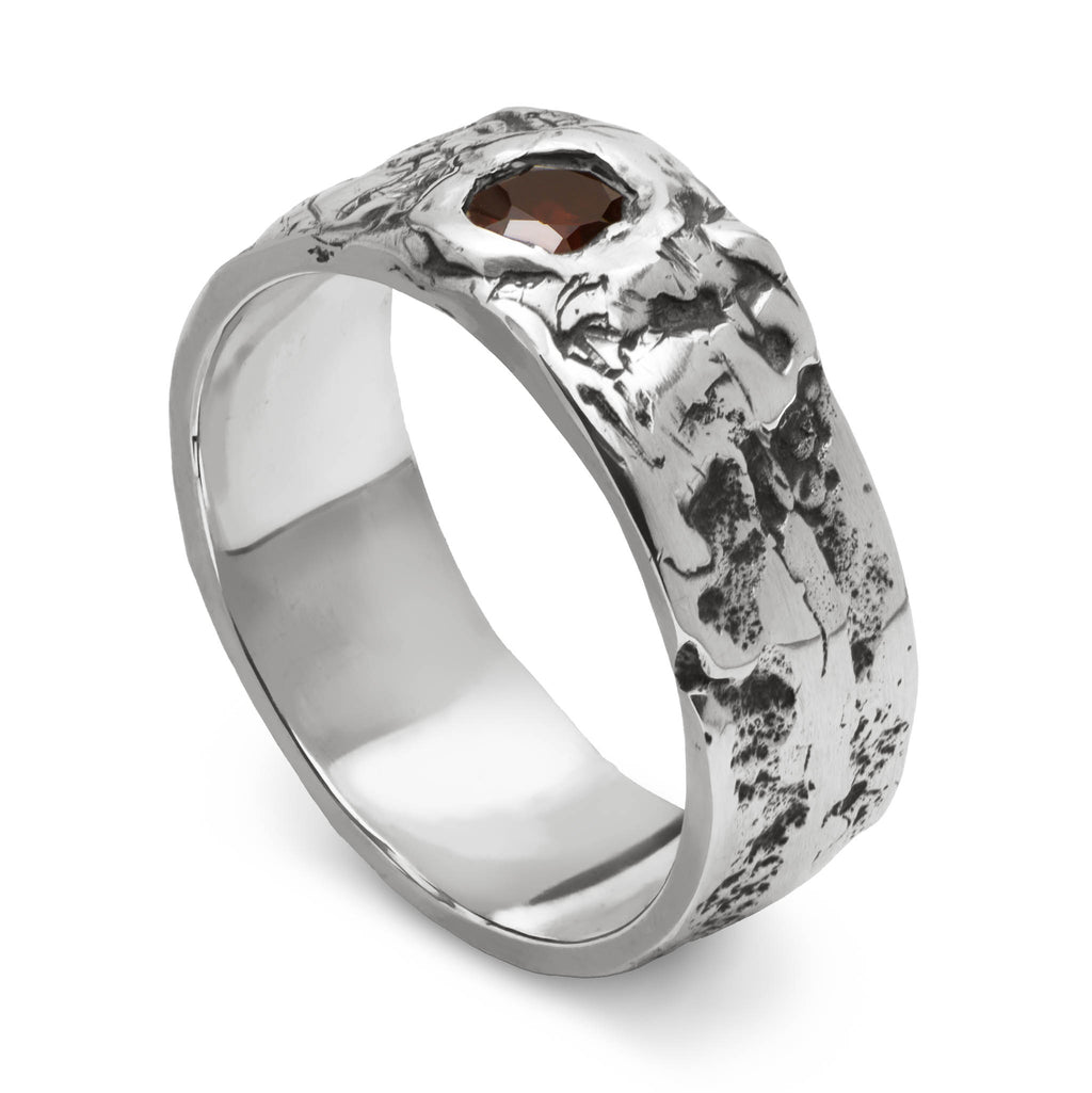 Sterling silver ring with red garnet and a rugged texture standing on a white background.