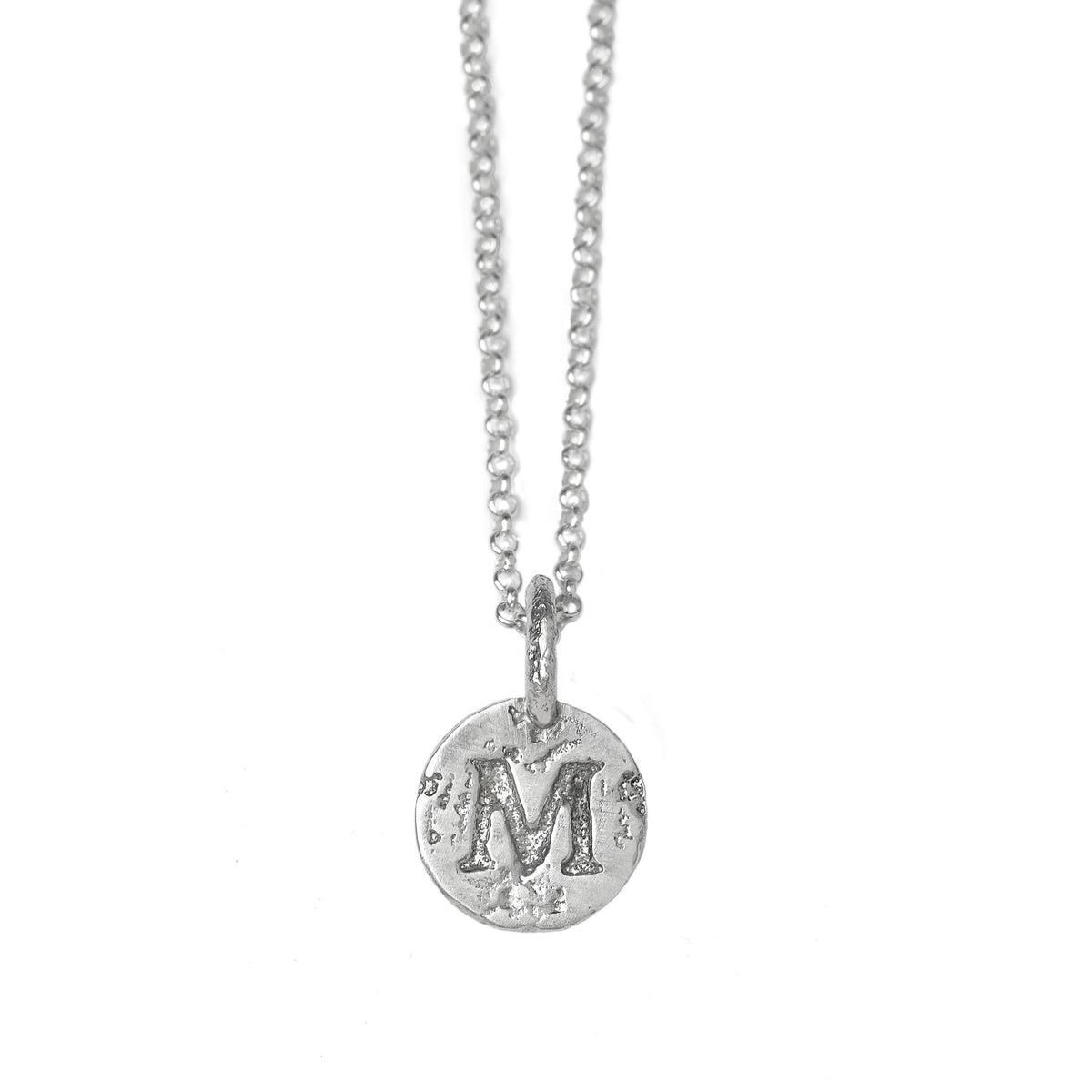 Handcrafted sterling silver initial coin necklace with personalised engraved round pendant hanginf from a silver chain against awhite background.