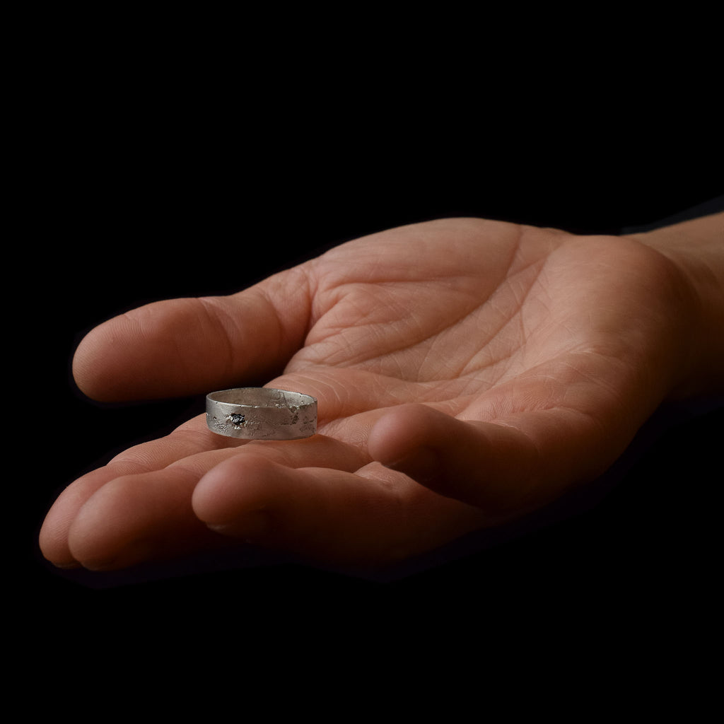A hand showing the kaewkosin ring with a black gemstone set in a textured silver band, handmade in berlin.