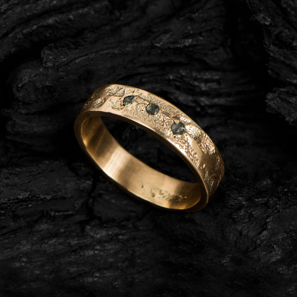Handcrafted wedding band in yellow gold with three tourmalines standing on a dark background.