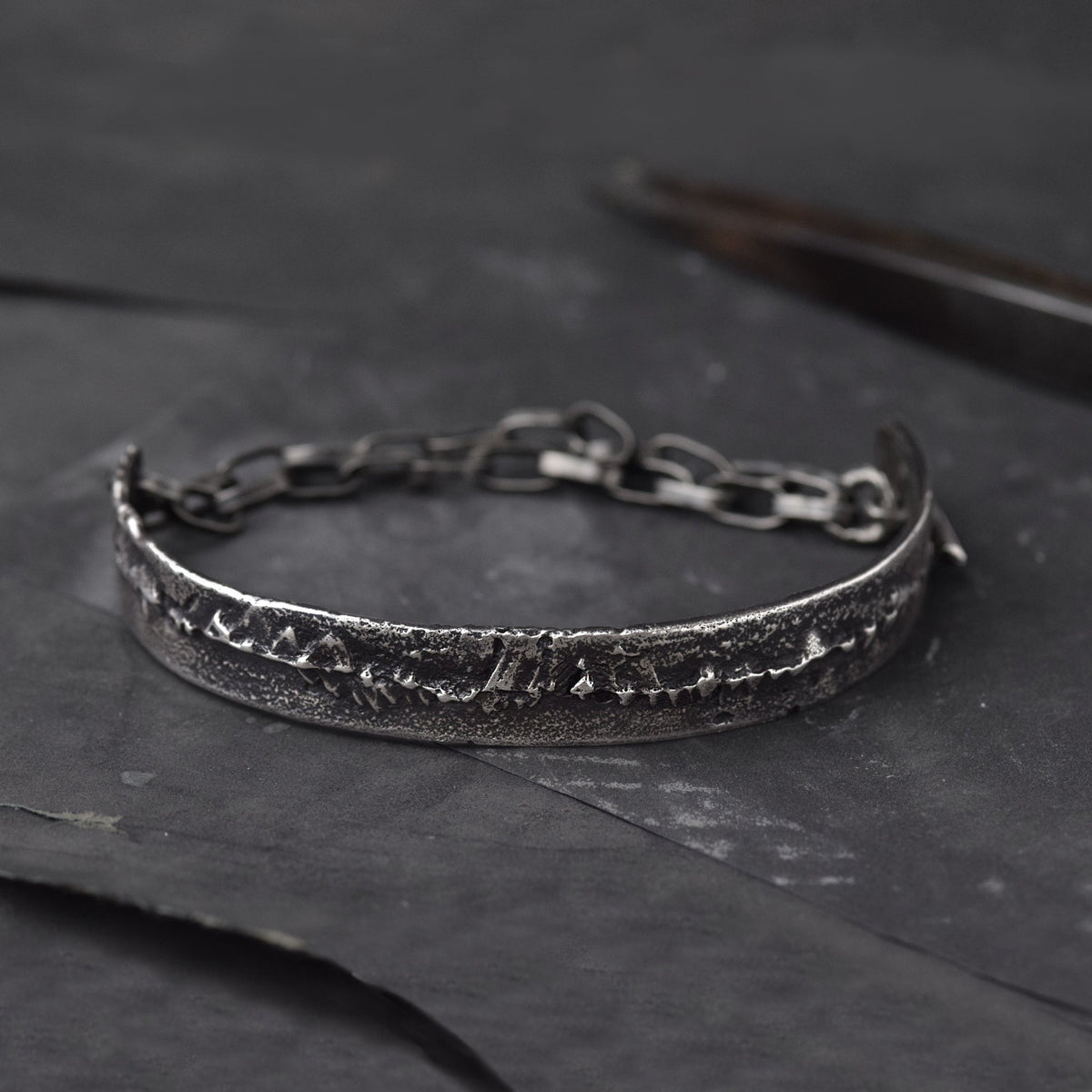 Mens cuff Bracelet in Sterling Silver, laying on a dark surface with some goldsmiths tools.