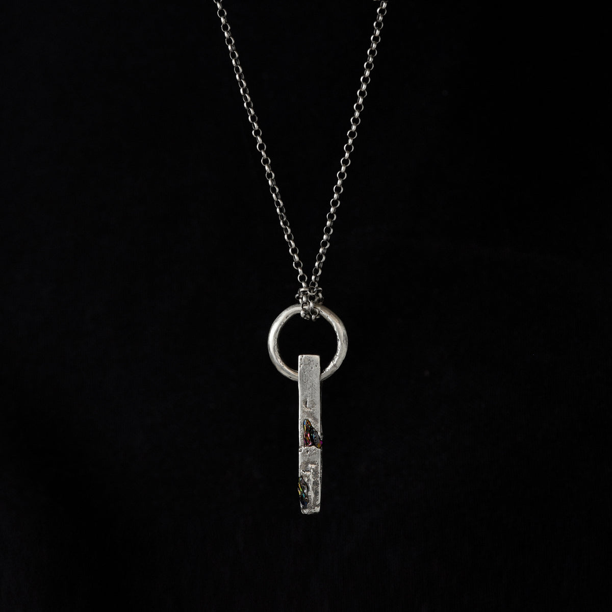 Handcrafted sterling silver necklace with sculptural bar pendant and suspended silver ring on a black bacrground