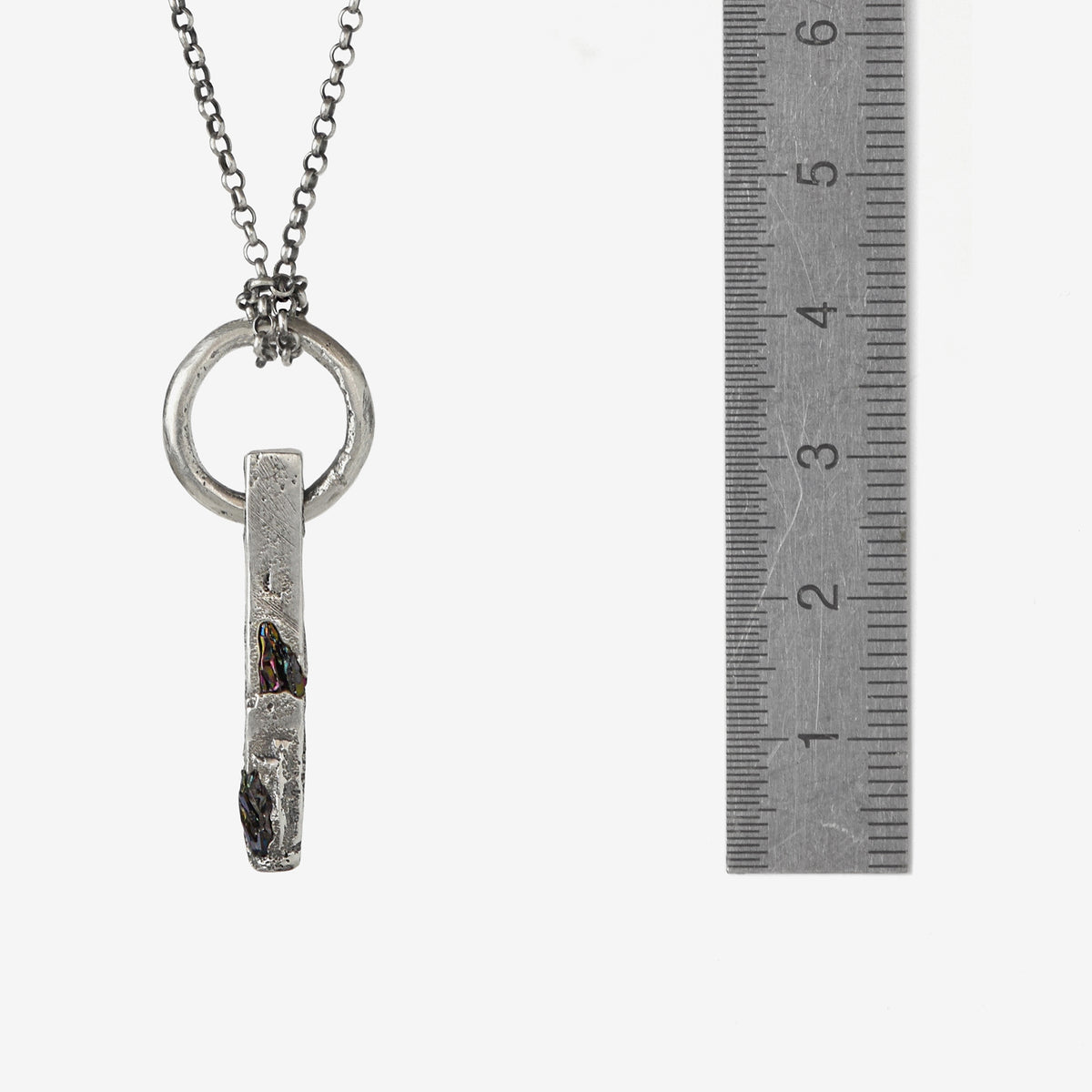 Handcrafted sterling silver necklace with sculptural bar pendant and suspended silver ring with aruler to show the size.