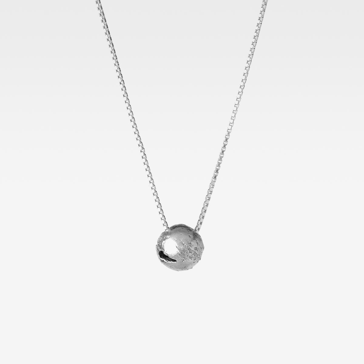 Suspended from a sterling silver curb chain hangs a handcrafted round pendant reminiscent of earth against a white background.