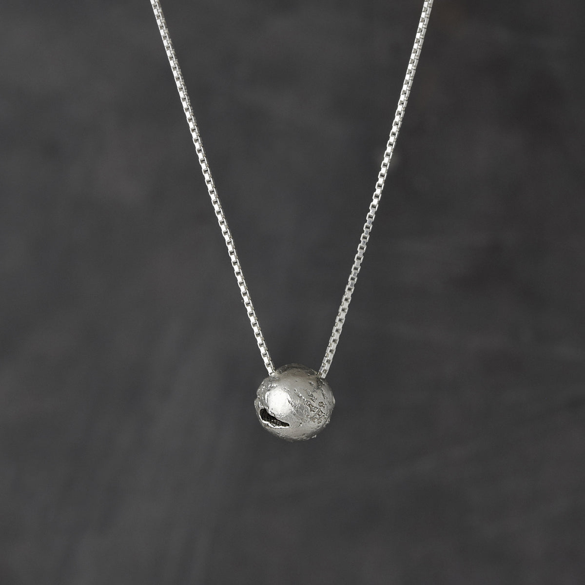 Suspended from a sterling silver chain hangs a handcrafted round pendant reminiscent of earth.