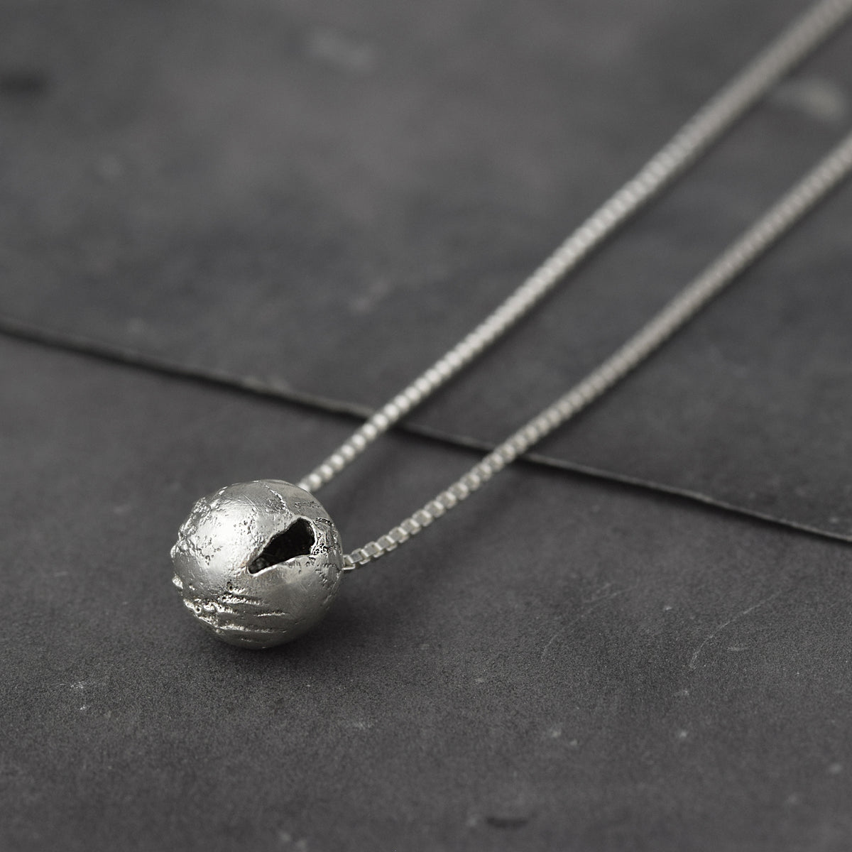 Handcrafted sterling silver hollow sphere pendant with a tactile finish suspended from a sterling silver chain.